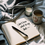 A journal flat lay on soft bedding with scattered prompts written like a lazy text message. Ambient glow. Moody but comforting.